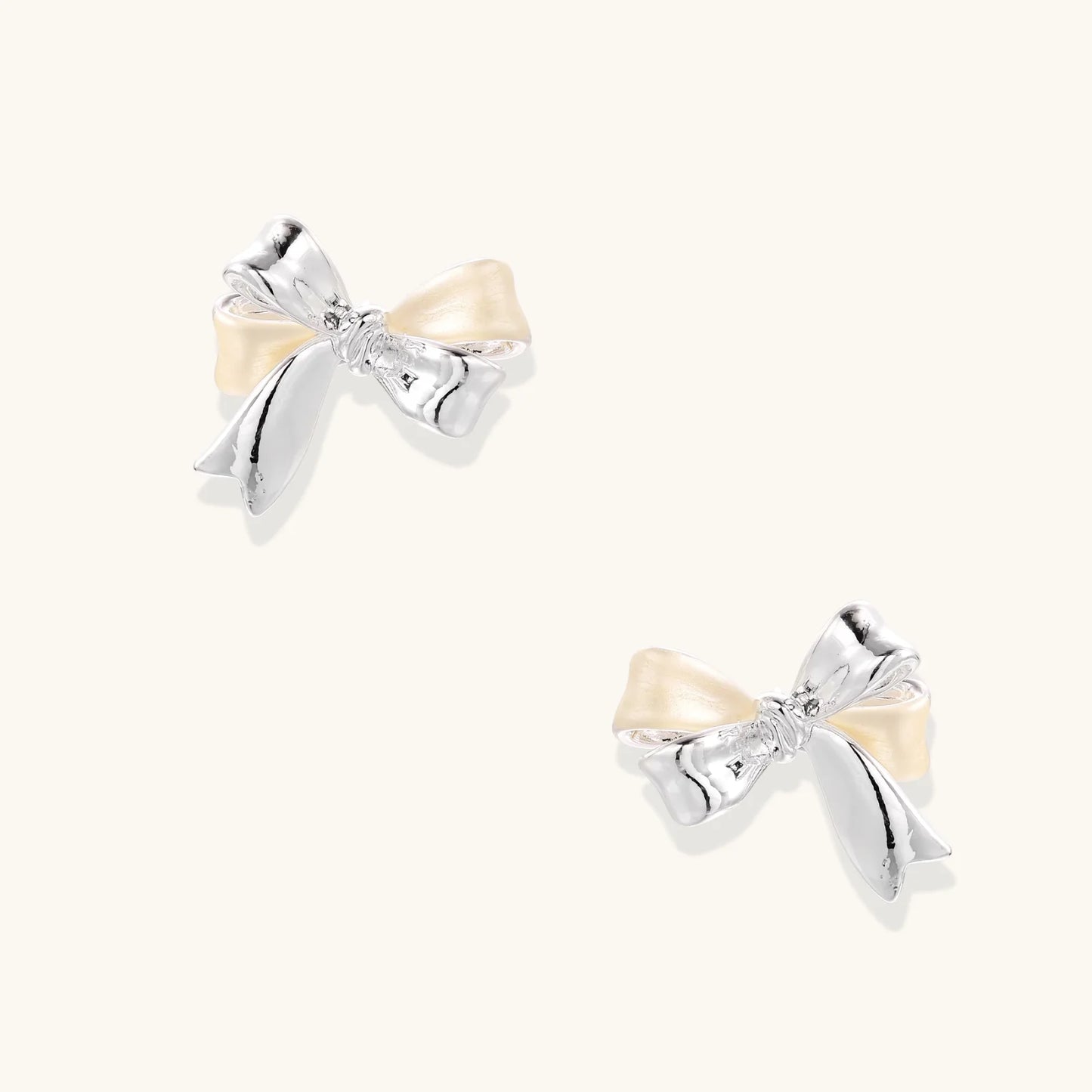 Dimensional bow stud earrings in white gold plated brass with silver and cream two-tone finish on neutral background