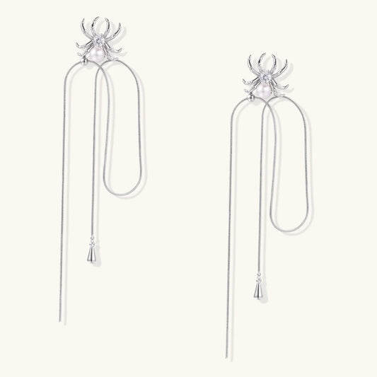 White gold plated spider earrings with pearl body and long threader chains on beige background