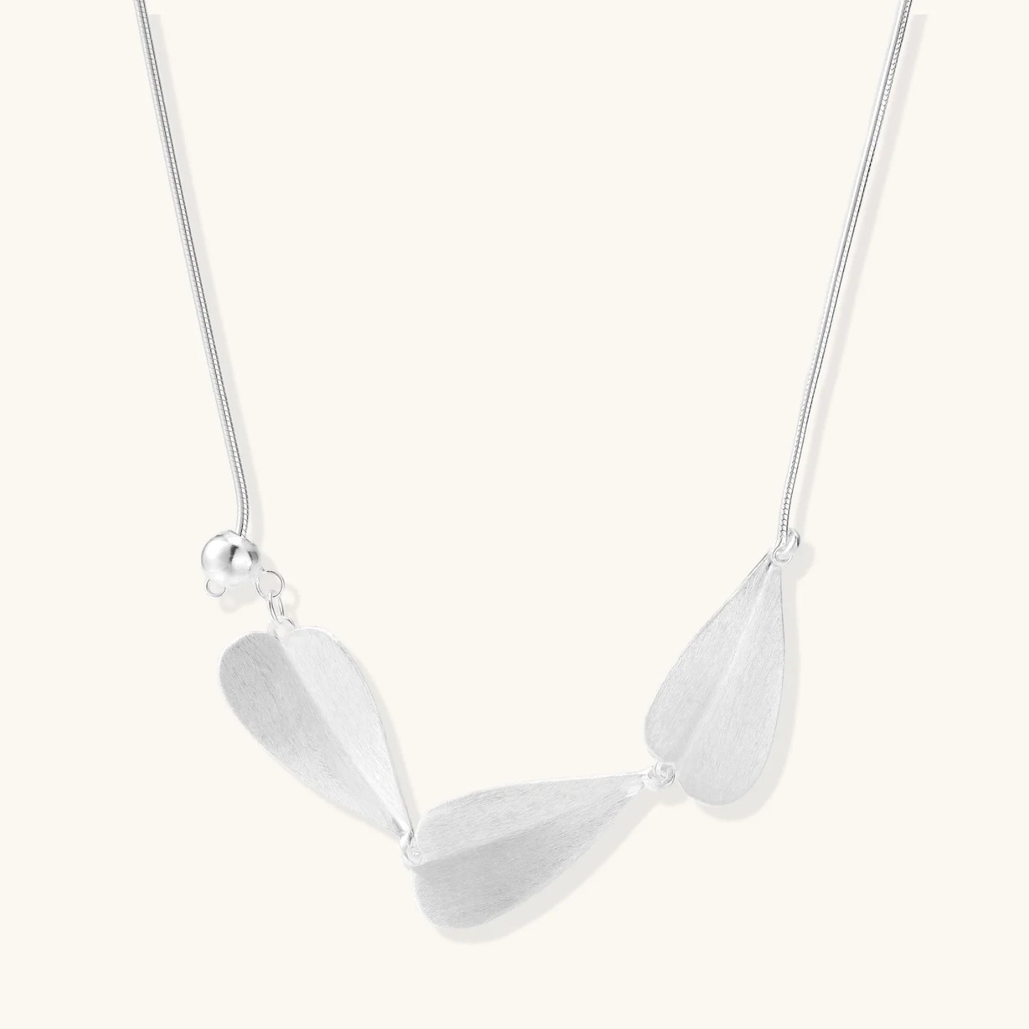 Minimalist sterling silver necklace with three brushed leaf-shaped pendants on delicate chain against white background
