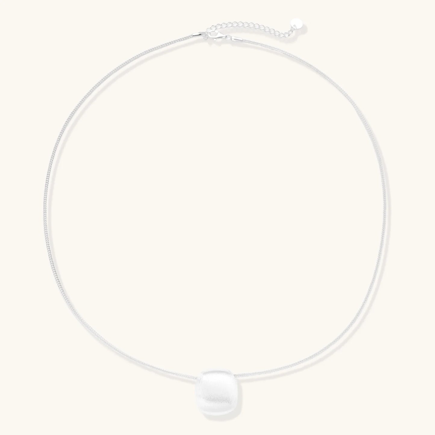 Minimalist brushed sterling silver dome pendant on delicate chain against cream background, showing matte textured finish