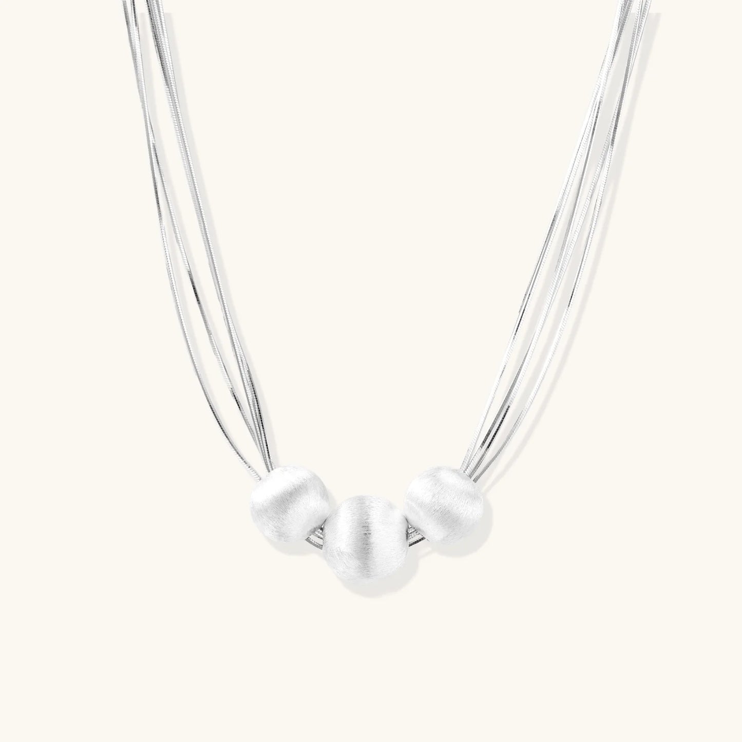 Sterling silver multi-strand necklace with three brushed round beads on cream background