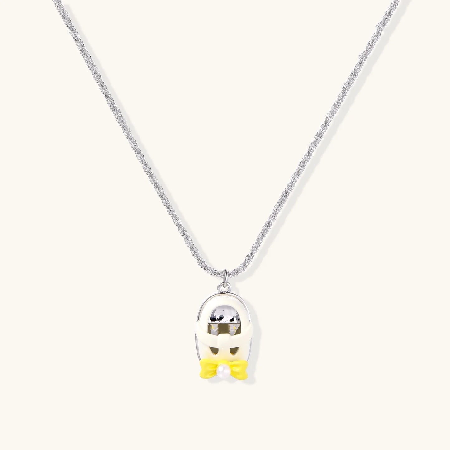 Chrome egg-shaped pendant with kawaii face, yellow bow, and pearl detail on silver chain against white background