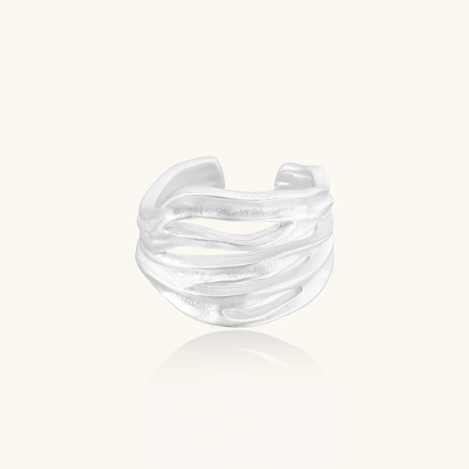 Wide sterling silver cuff ring with flowing wave patterns creating dimensional texture against cream background