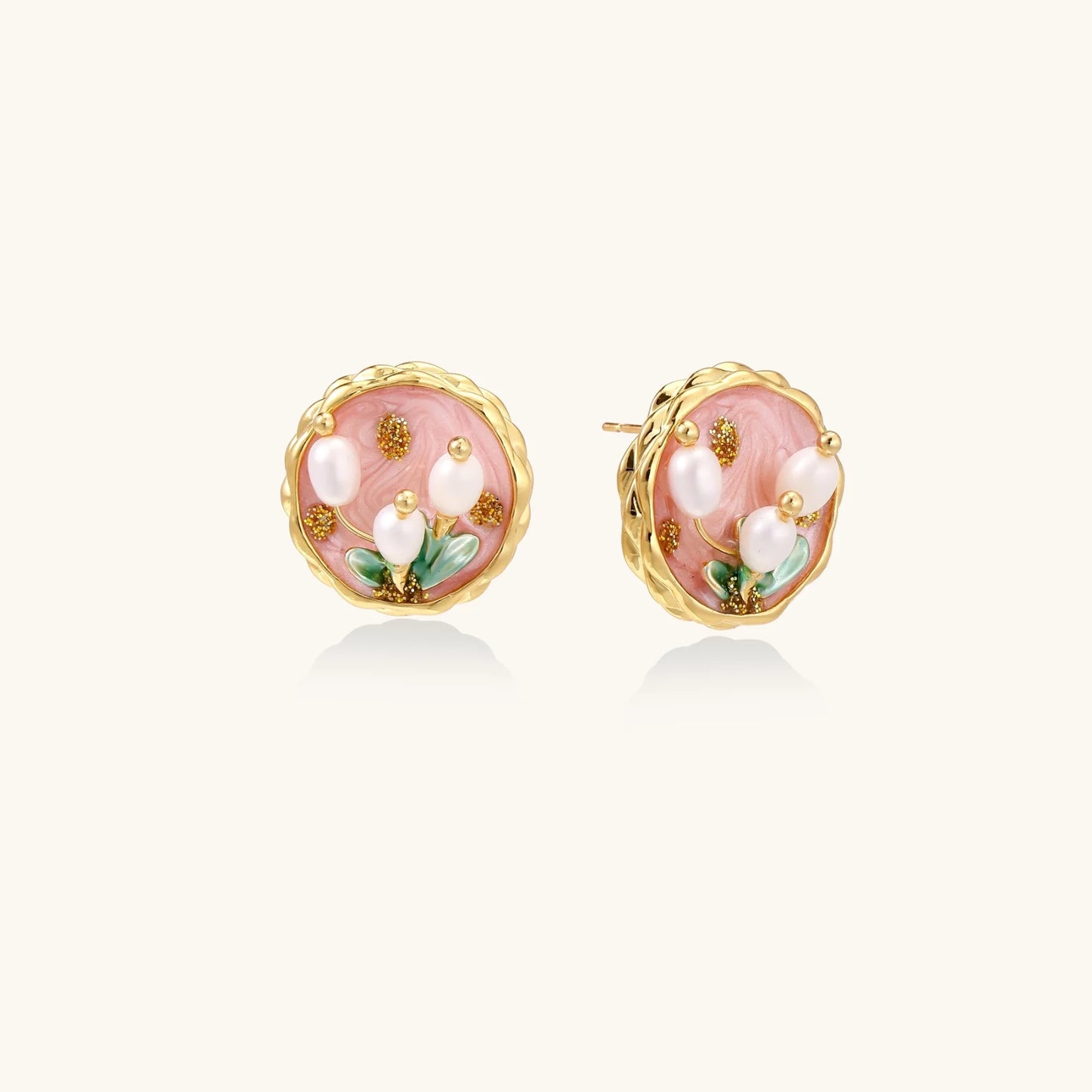 Round stud earrings with pink enamel, three white freshwater pearls, green leaves, and gold-plated braided border