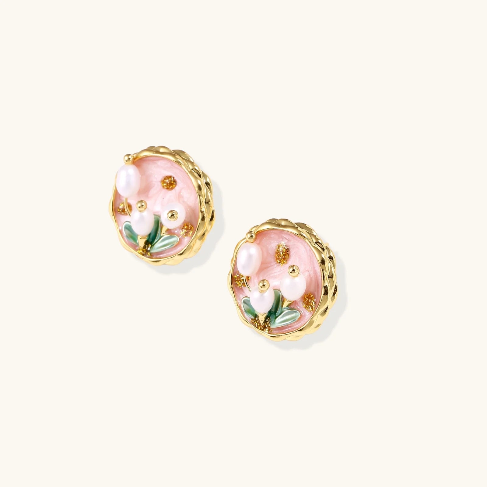 Round stud earrings with pink enamel, three white freshwater pearls, green leaves, and gold-plated braided border