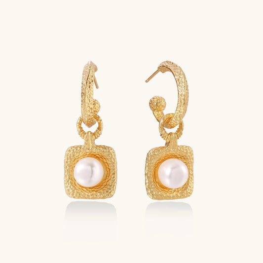 Pair of gold vermeil hoop earrings with textured square frames holding freshwater pearls on cream background