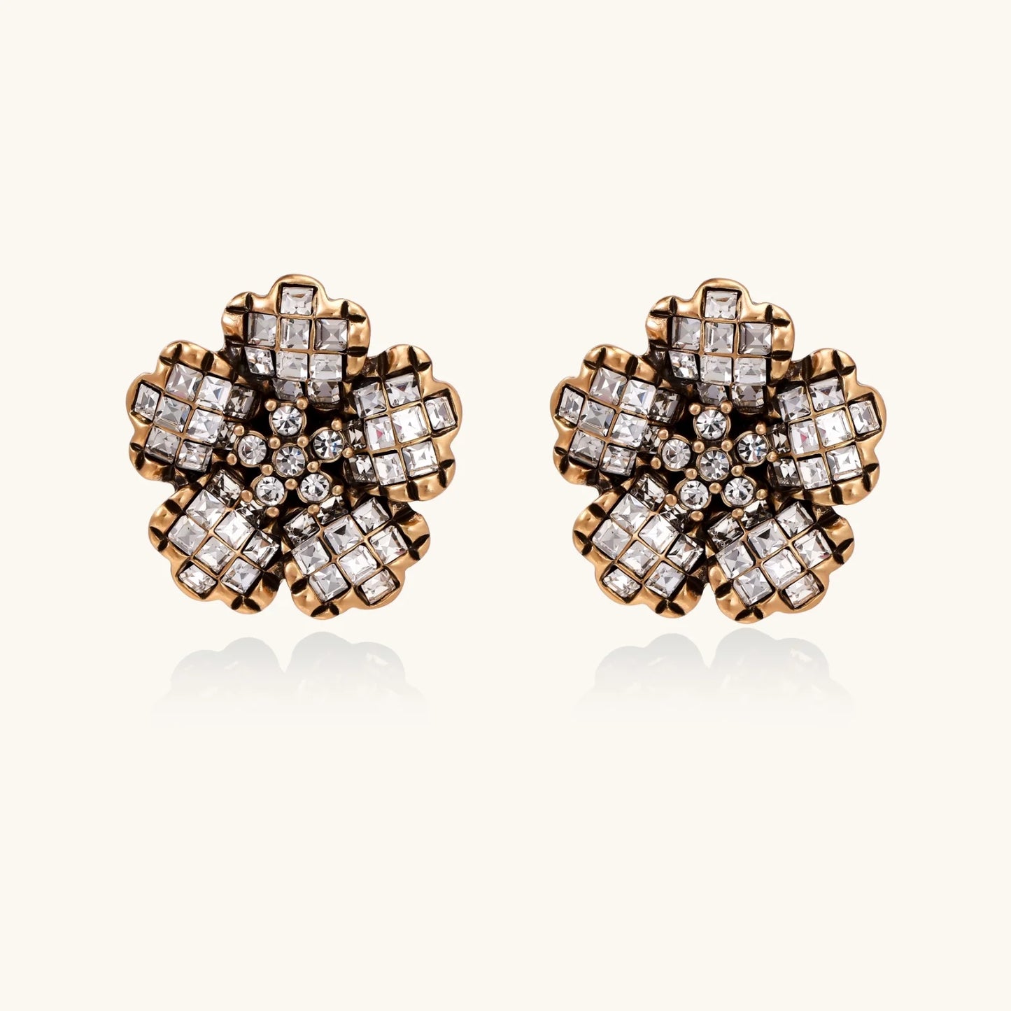 Gold-plated floral stud earrings with geometric zirconia crystals arranged in five-petal design on cream background