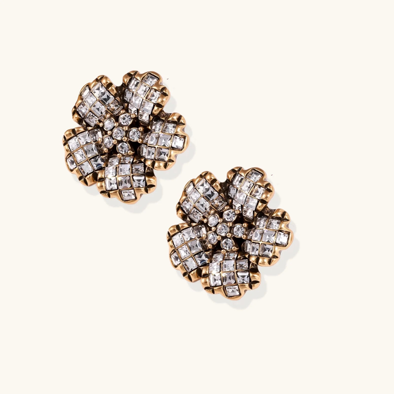 Gold-plated floral stud earrings with geometric zirconia crystals arranged in five-petal design on cream background