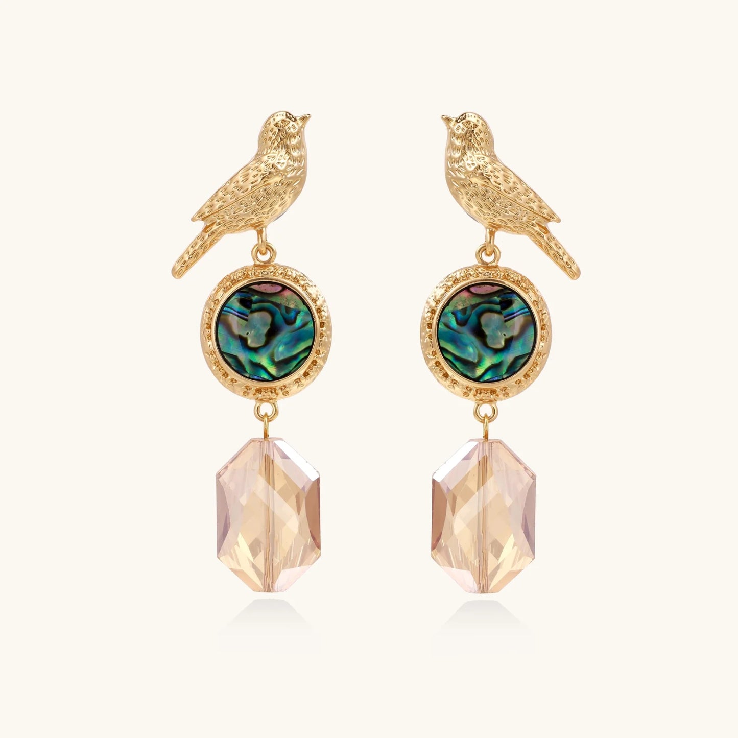 Gold-plated bird stud earrings with iridescent abalone shell medallions and champagne crystal drops on cream background
