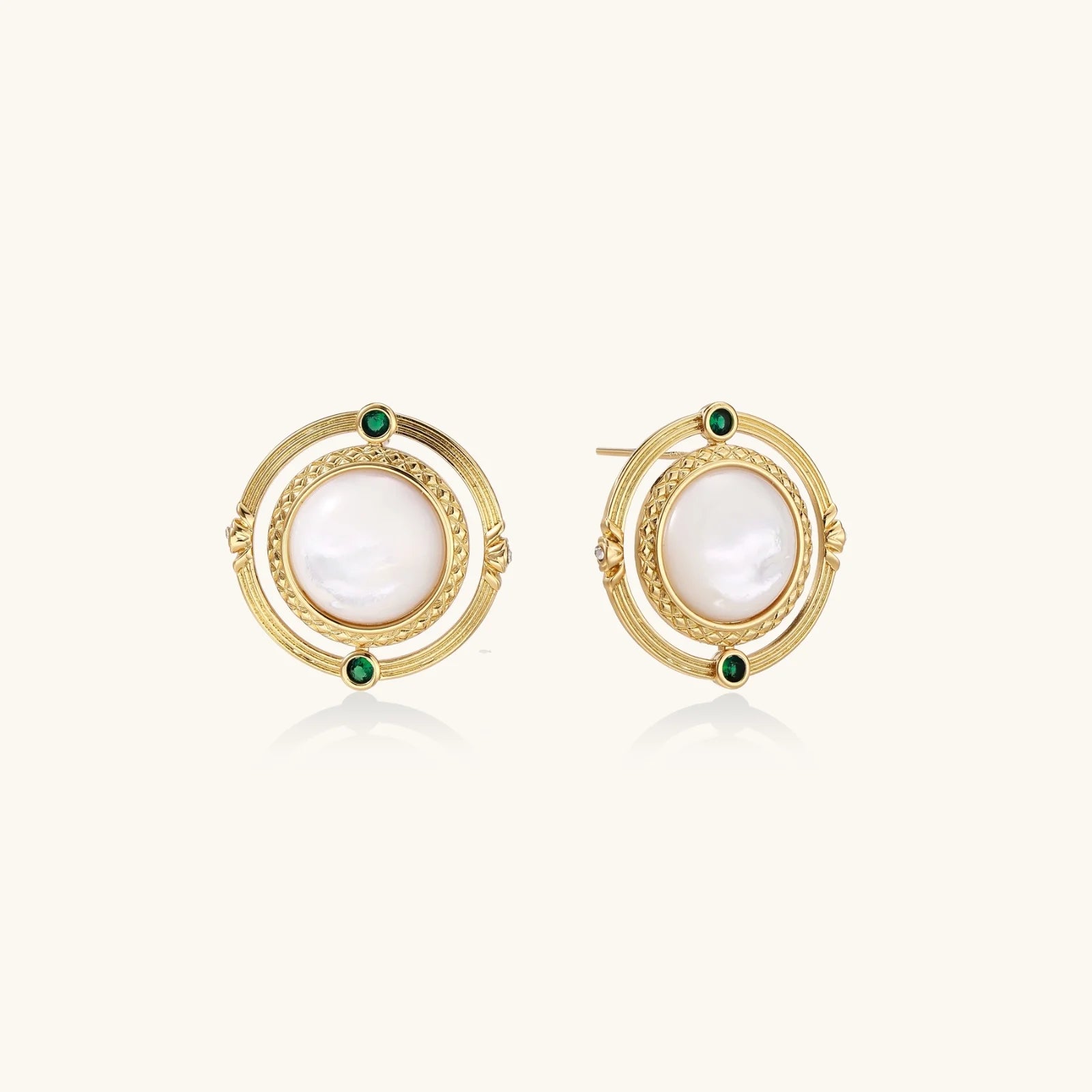 Circular gold stud earrings with iridescent mother-of-pearl center and green zirconia accents on cream background.