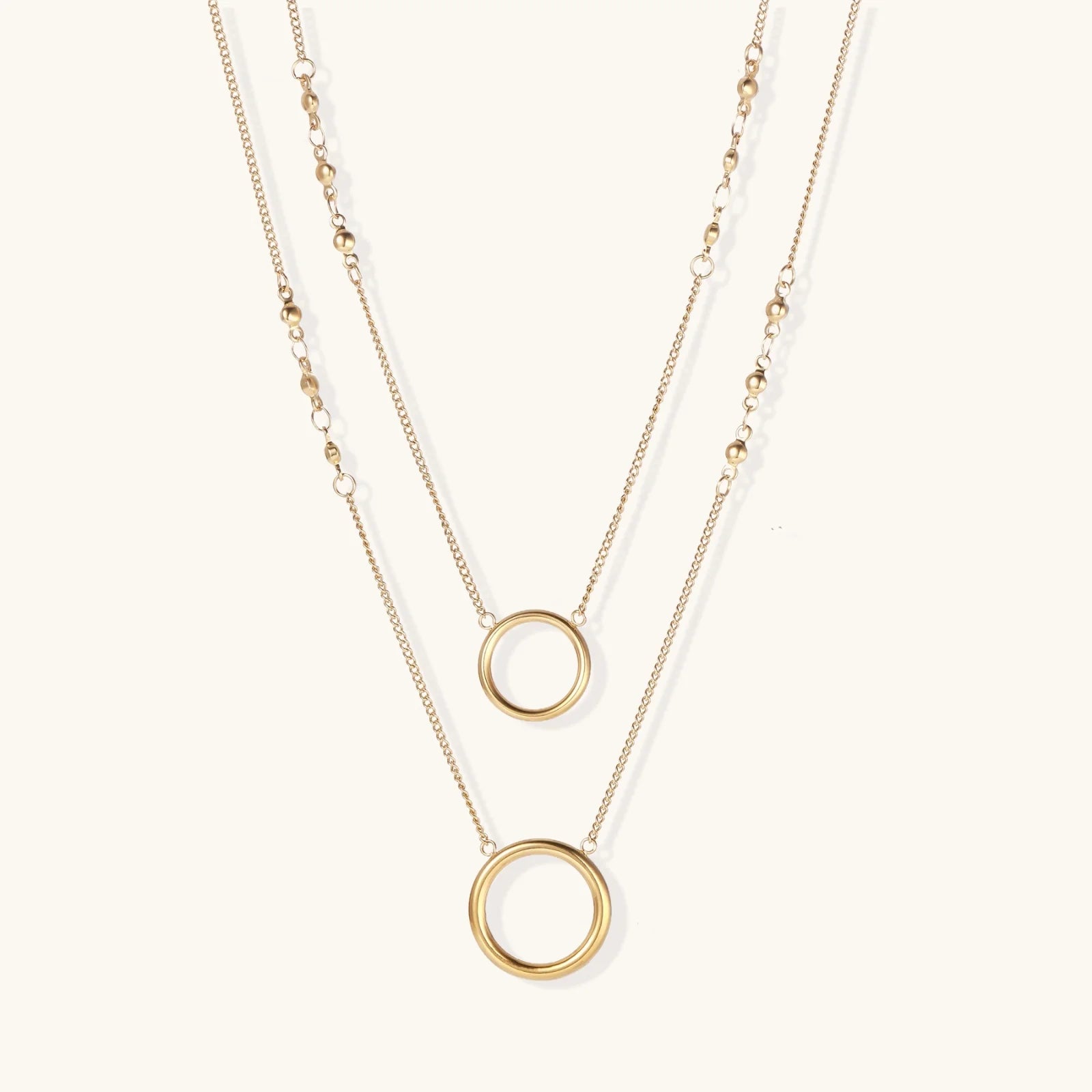 Layered gold necklace set with two open circle pendants and mixed chain styles on beige background