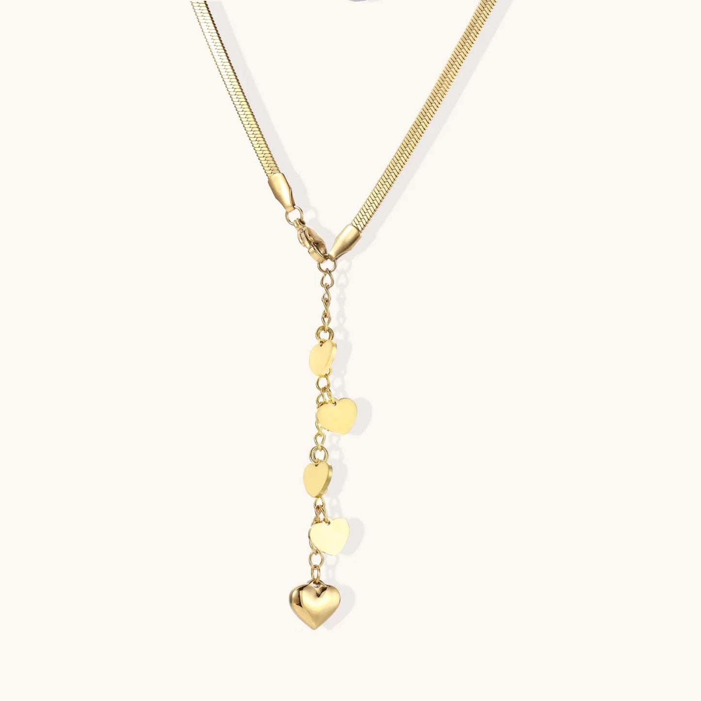 Gold Y-shaped necklace with five graduated heart charms cascading down a herringbone chain on white background