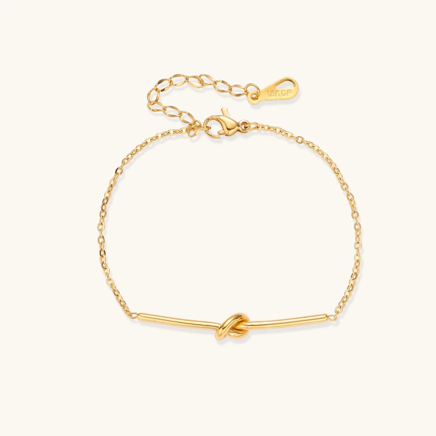 Delicate gold chain bracelet with minimalist bar and centered knot detail on cream background