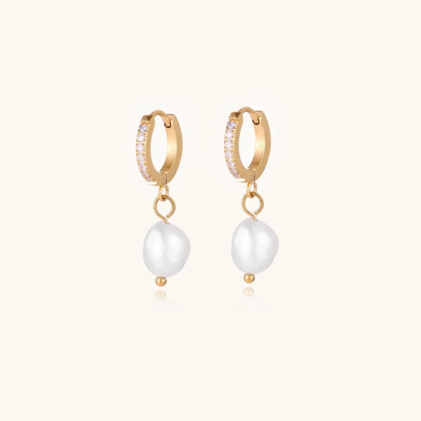 Gold huggie hoop earrings with pavé crystals and white freshwater pearl drops on cream background