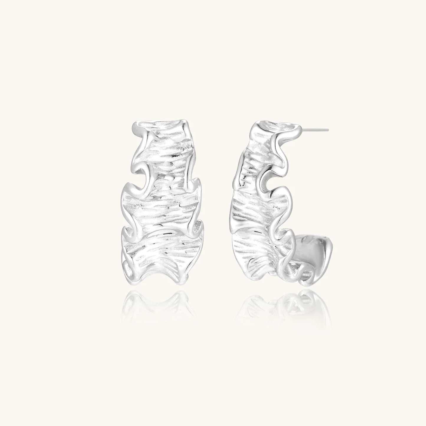 White gold plated sculptural hoop earrings with organic wavy edges and reflective metallic finish on cream background