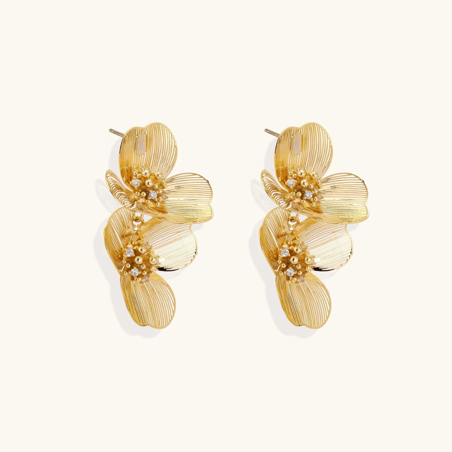 Pair of gold-plated double flower earrings with textured petals and crystal centers on cream background.