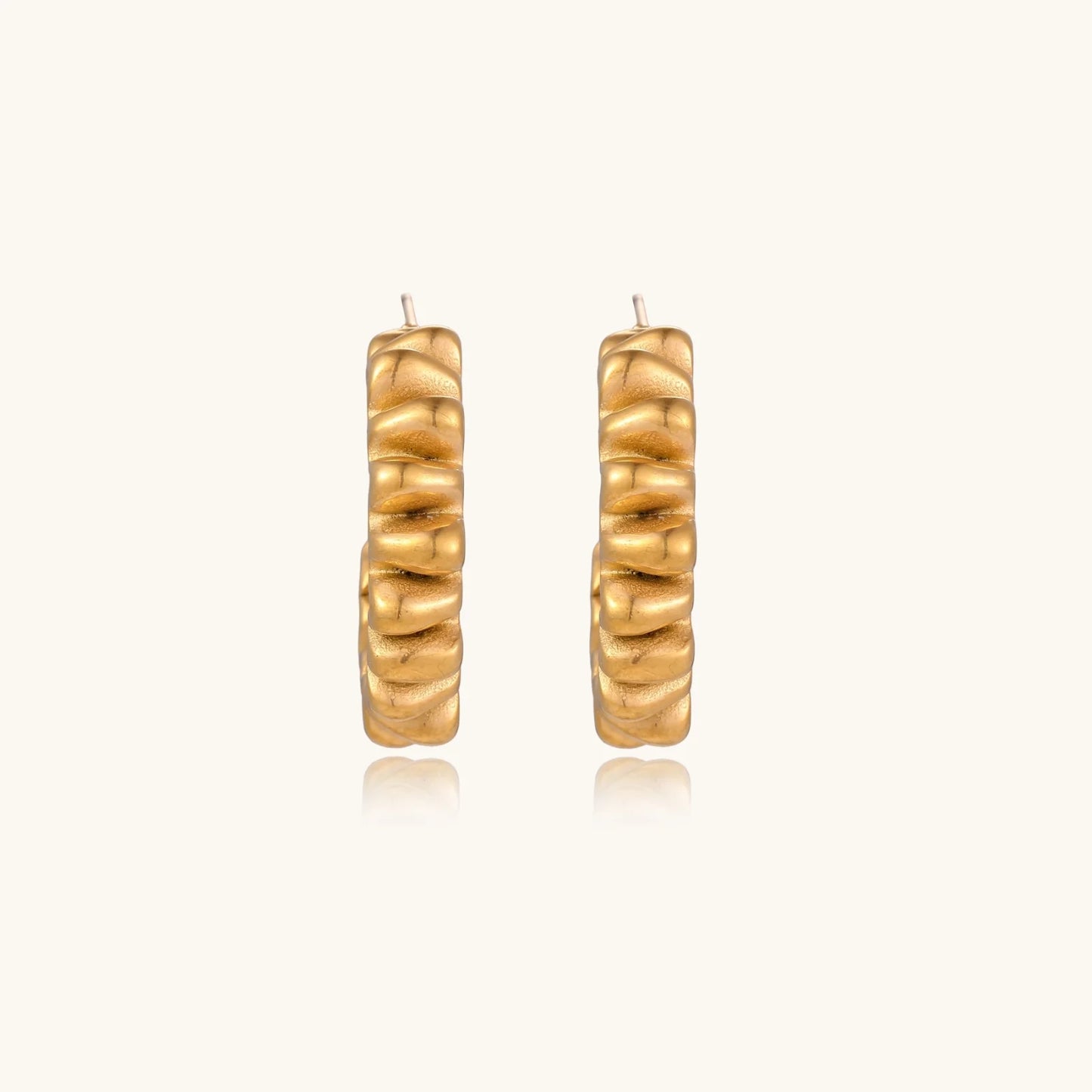 Sculptural gold-plated hoop earrings with continuous twisted spiral design on cream background