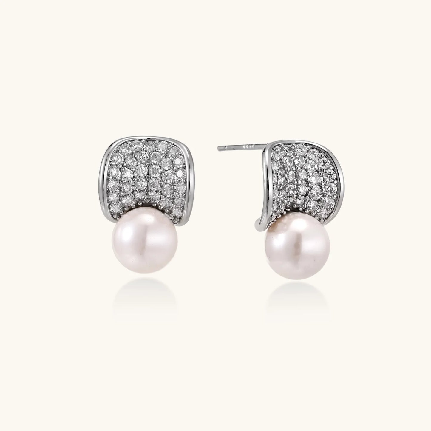 Curved pavé diamond studs in white gold-plated brass cradle lustrous freshwater pearls against cream background