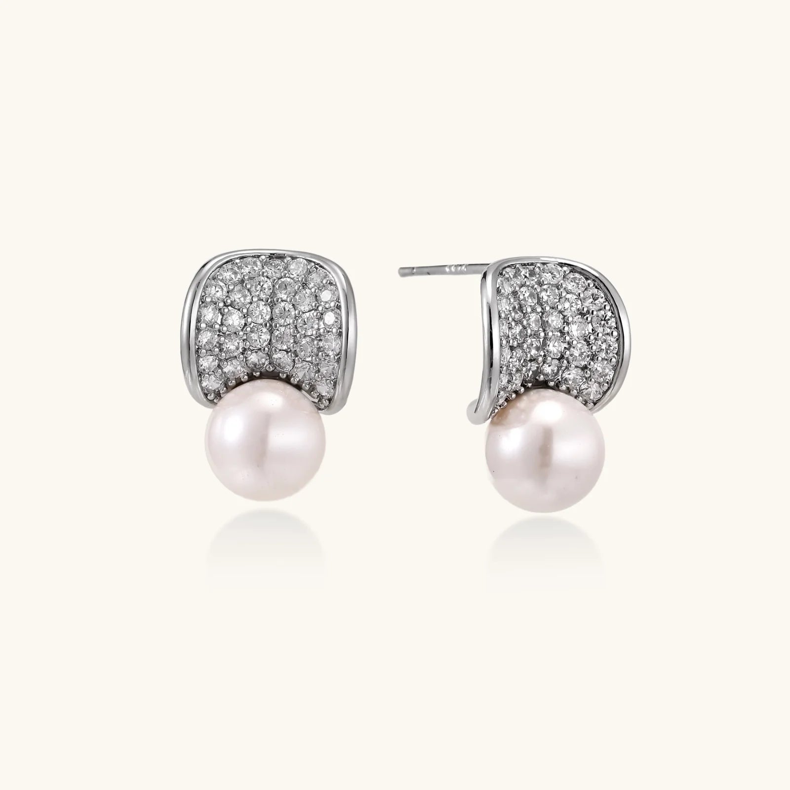 Curved pavé diamond studs in white gold-plated brass cradle lustrous freshwater pearls against cream background