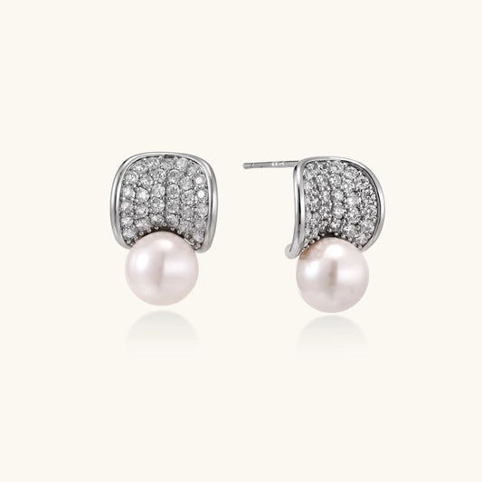 Curved pavé diamond studs in white gold-plated brass cradle lustrous freshwater pearls against cream background