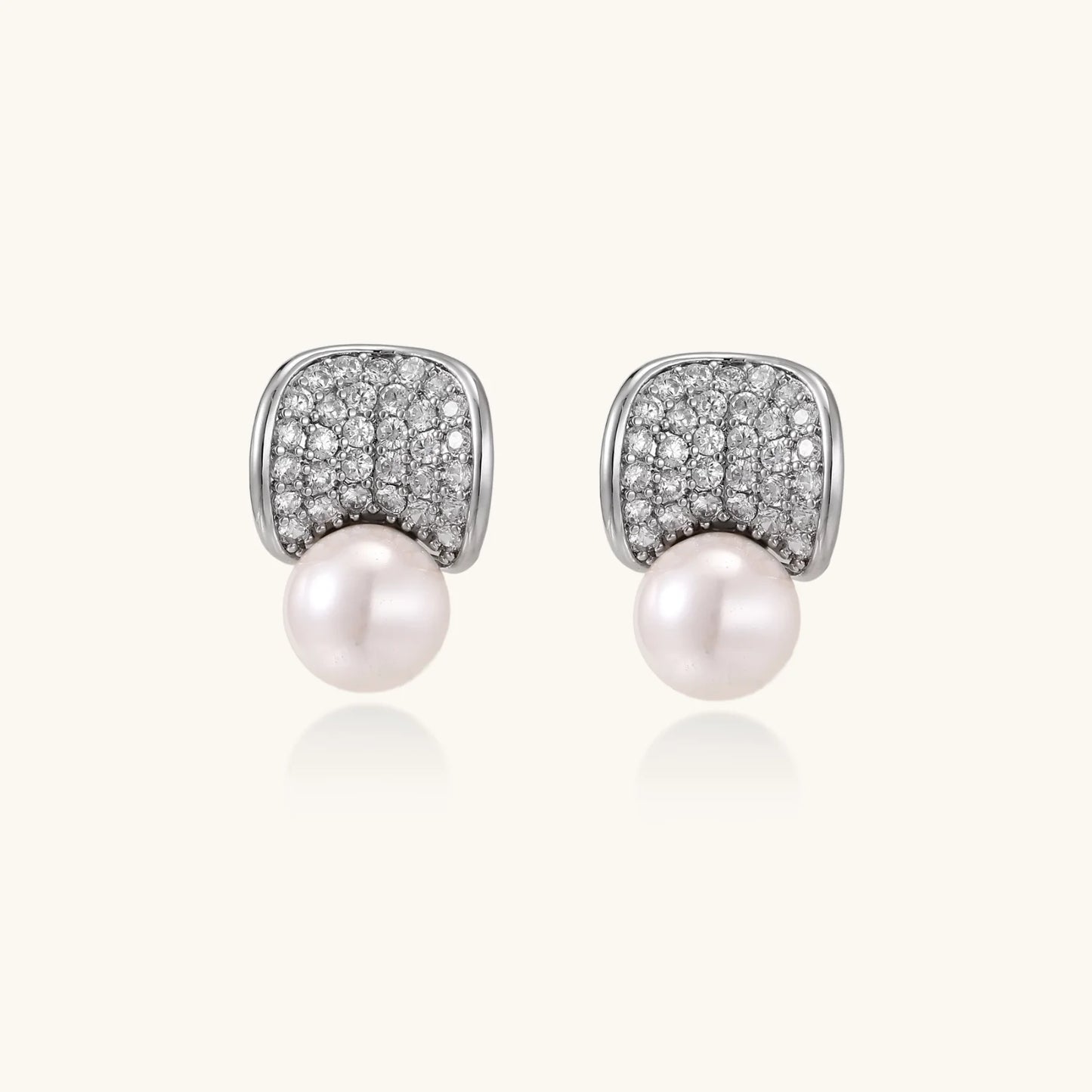 Curved pavé diamond studs in white gold-plated brass cradle lustrous freshwater pearls against cream background