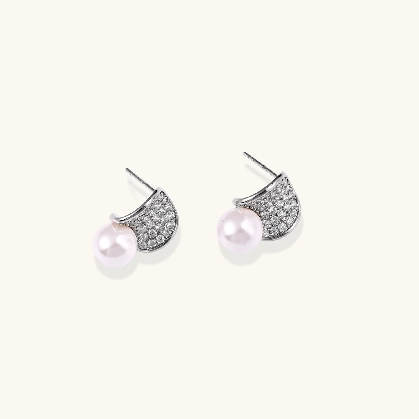 Curved pavé diamond studs in white gold-plated brass cradle lustrous freshwater pearls against cream background
