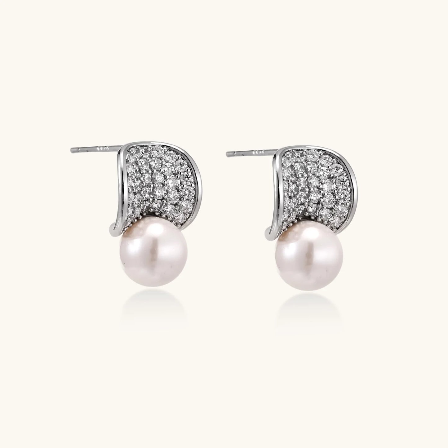 Curved pavé diamond studs in white gold-plated brass cradle lustrous freshwater pearls against cream background