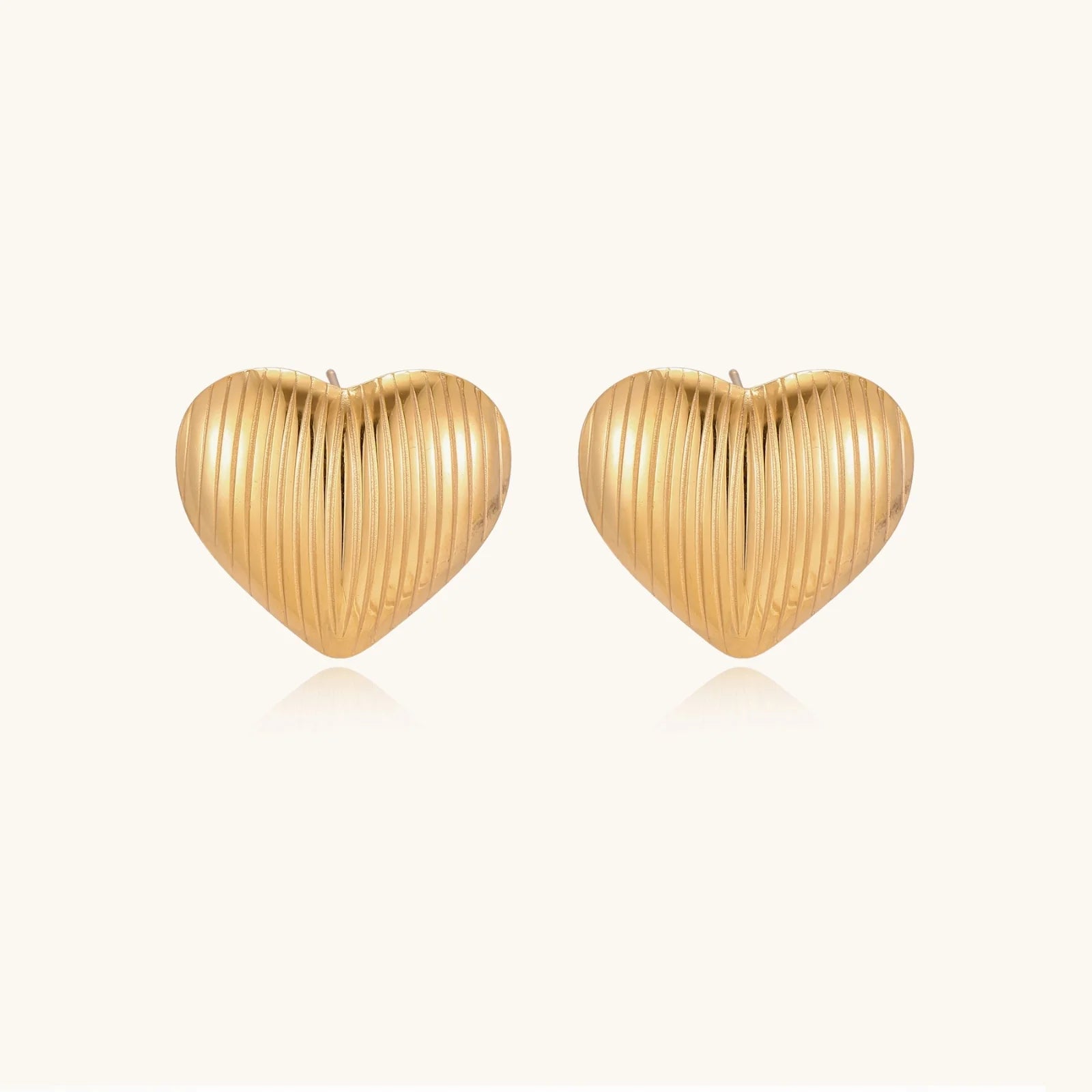 Gold heart-shaped stud earrings with parallel ridged texture on cream background