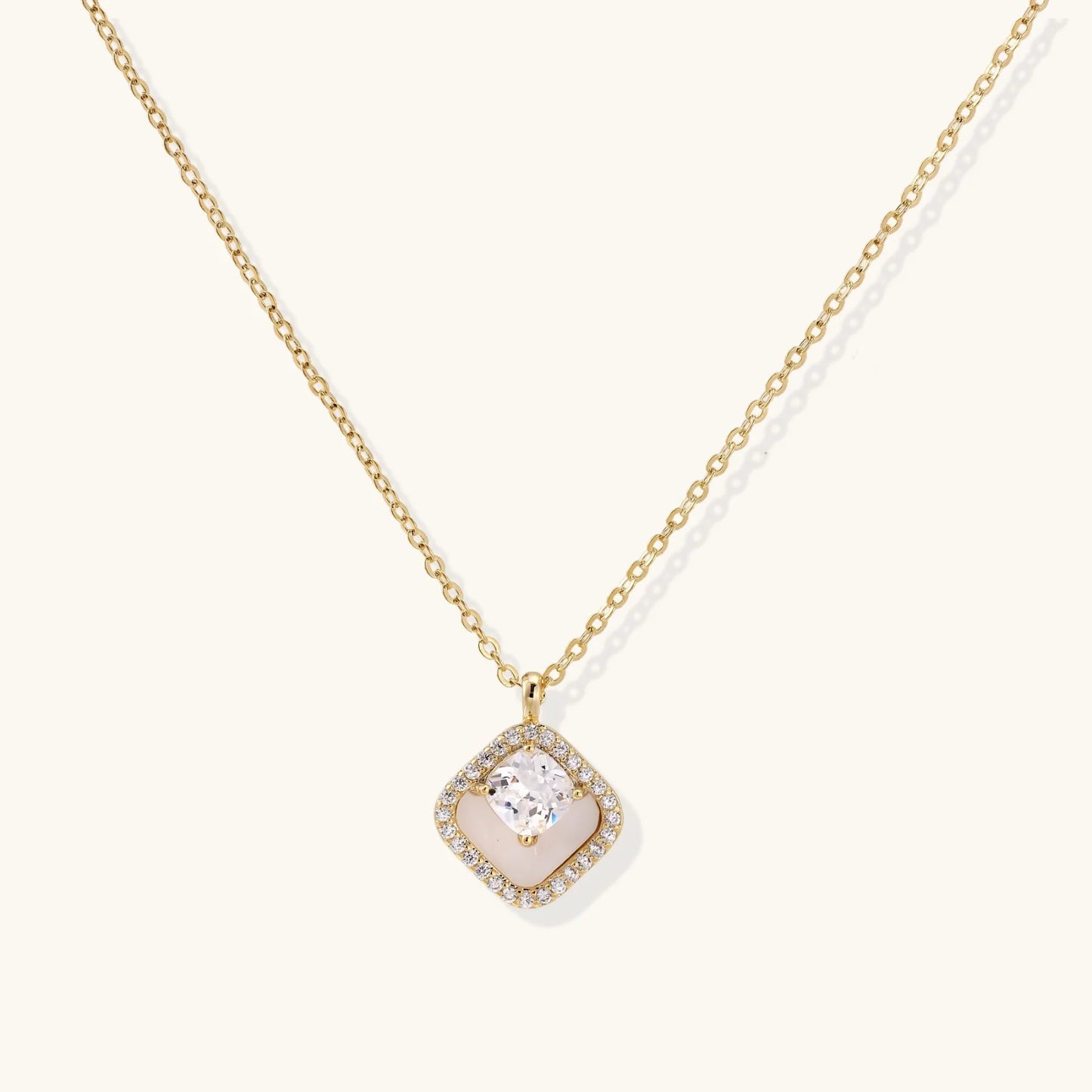 Gold quatrefoil pendant with crystal center on iridescent mother-of-pearl base, adjustable gold chain on cream background