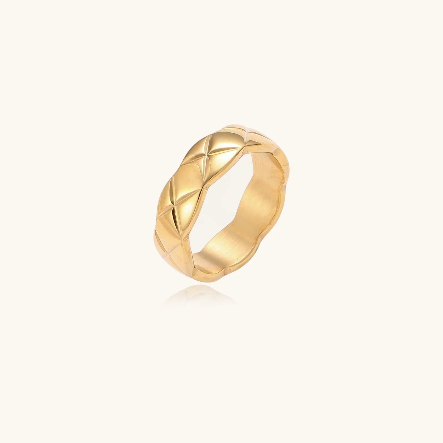 Close-up of an 18K gold-plated twisted band ring with dimensional braided pattern on cream background.