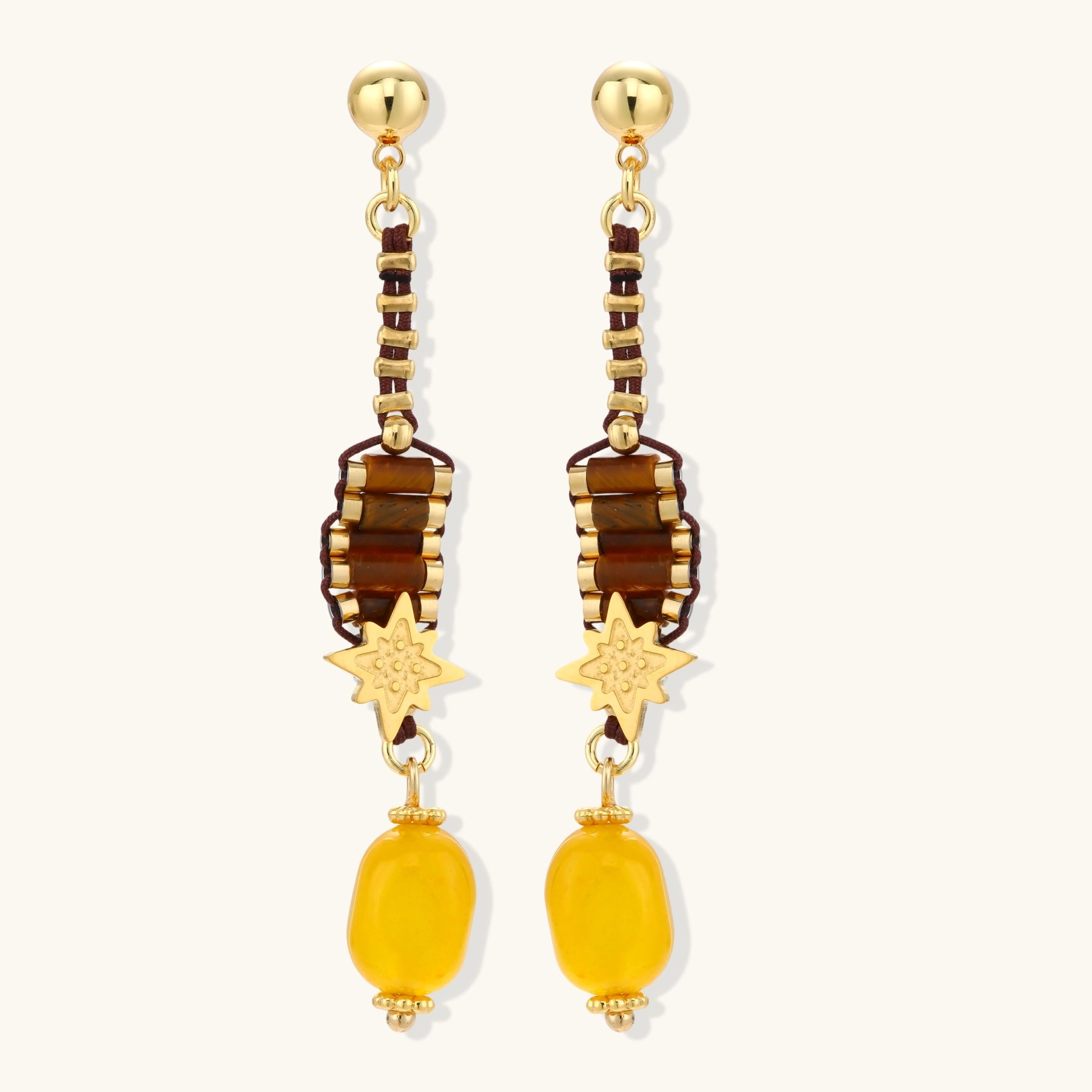 Gold-plated dangle earrings with brown gemstones, star charms, and yellow amber drops on cream background.
