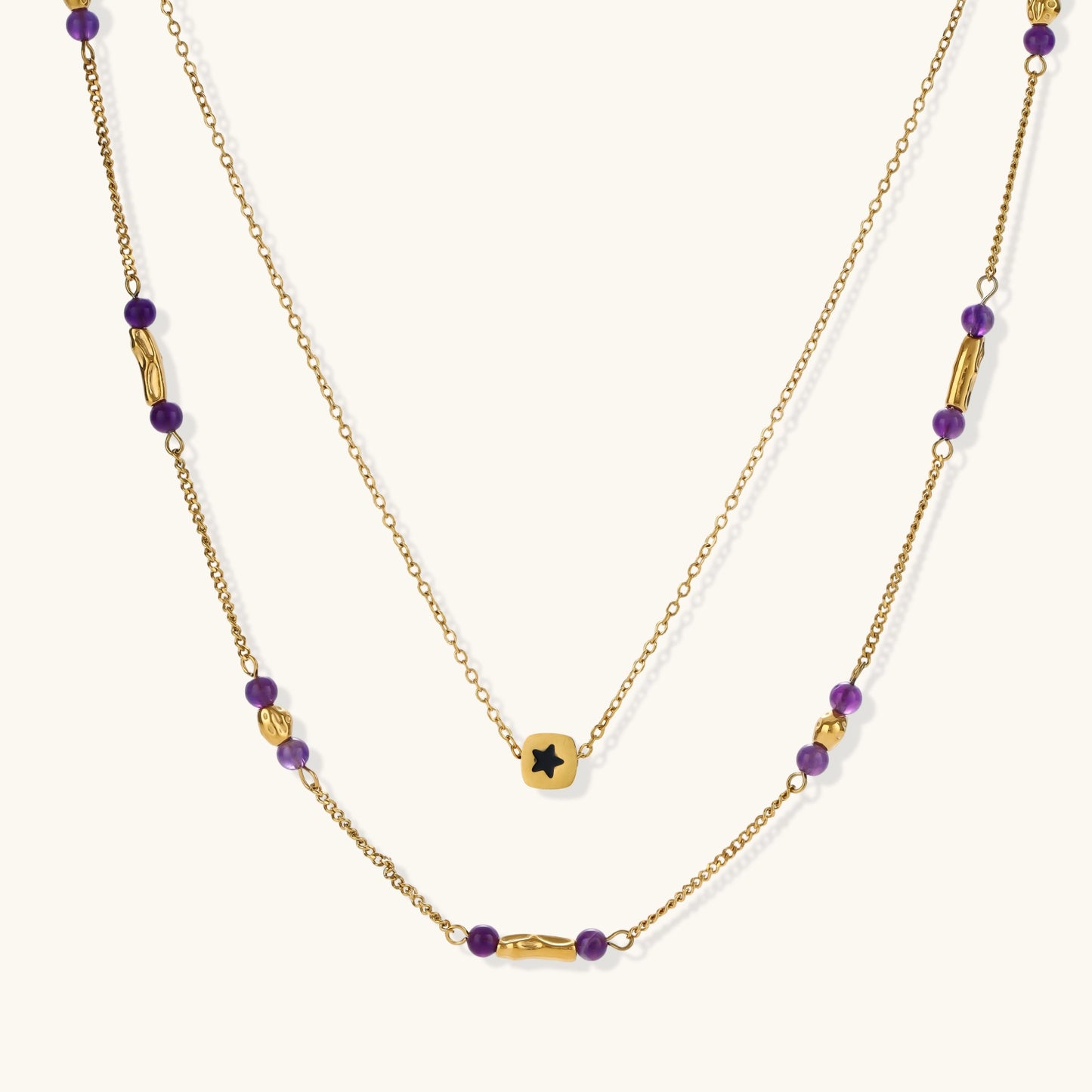 Two layered gold-tone necklaces with purple stone beads and star pendant against cream background.