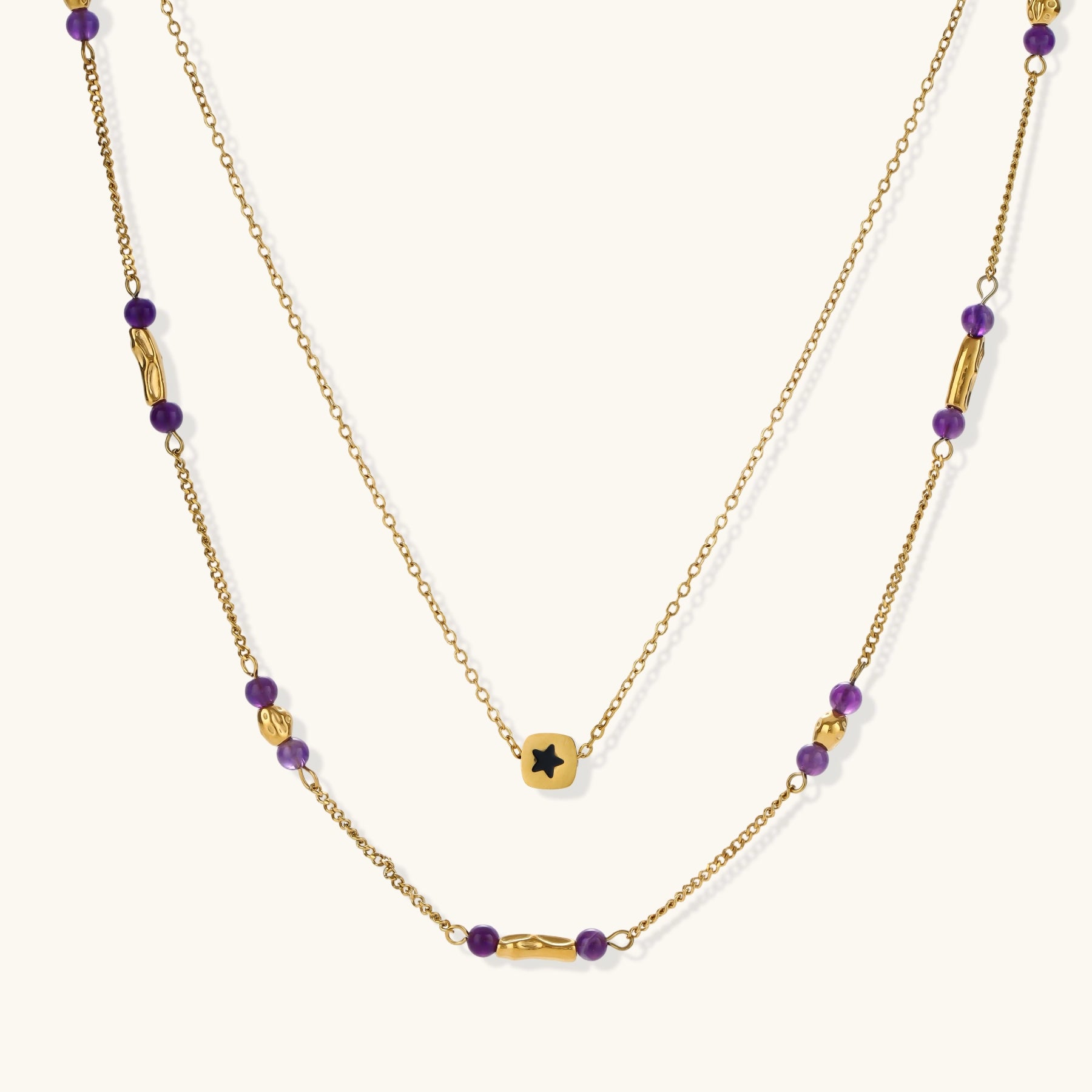 Two layered gold-tone necklaces with purple stone beads and star pendant against cream background.