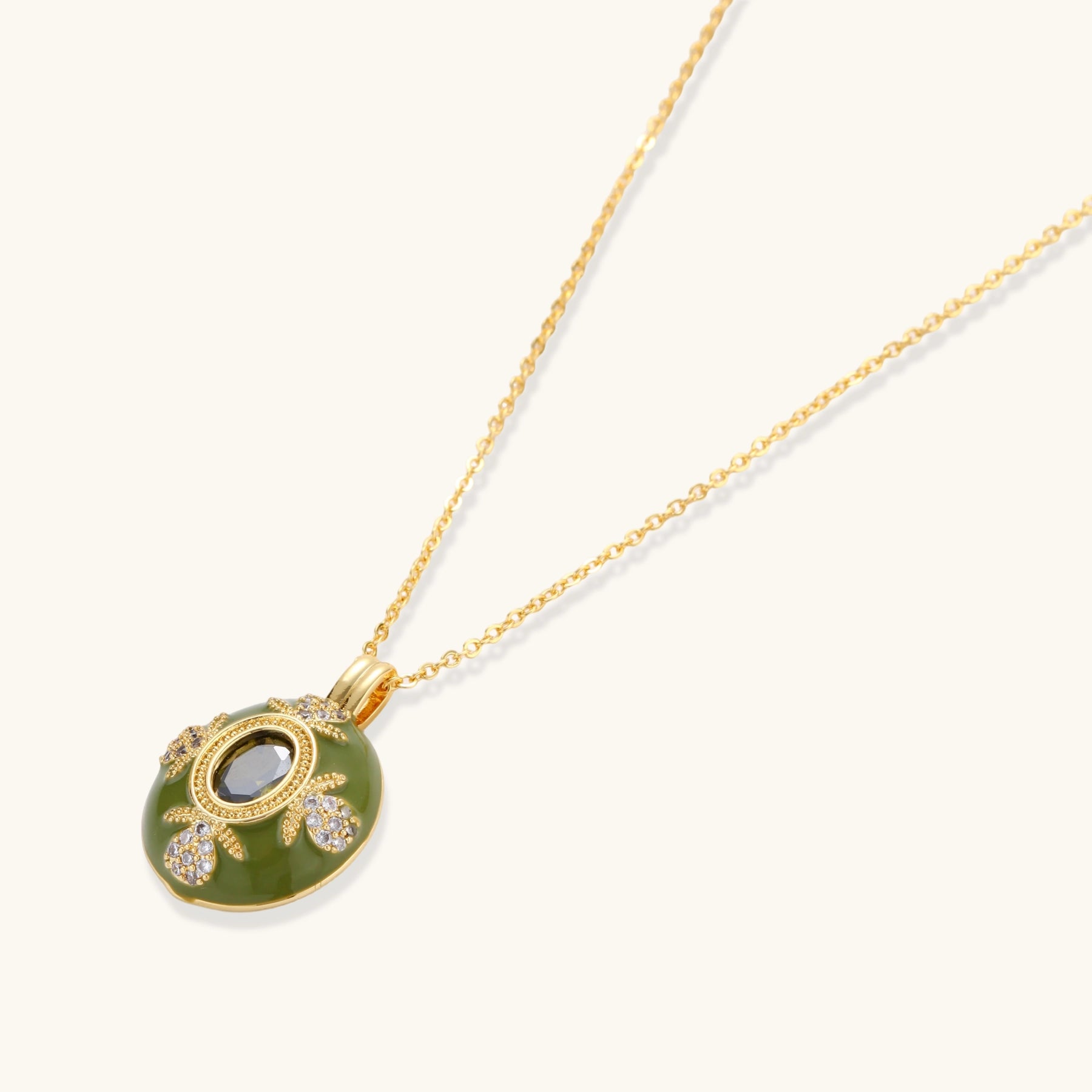 Gold-plated pendant necklace with green enamel background and oval olive cubic zirconia center stone with crystal accents.